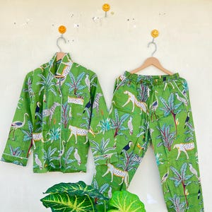 May include: Green pajama set with a jungle print featuring leopards, toucans, and palm trees. The top has a button-up closure and long sleeves. The pants have an elastic waistband.