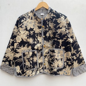 Könnte beinhalten: Eine schwarze und cremefarbene, gesteppte Jacke mit Blumenmuster, einem Stehkragen und Knopfverschluss. Die Jacke hat zwei aufgesetzte Taschen und einen gestreiften Saum.