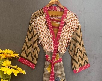 Può includere: Una lunga veste rosa e marrone con motivo a fantasia e una cintura. La veste ha un motivo geometrico sulle maniche e un motivo floreale con ballerini sul davanti.
