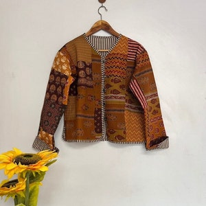 May include: A brown quilted jacket with a patchwork design featuring various patterns and colours. The jacket has a button closure and long sleeves.