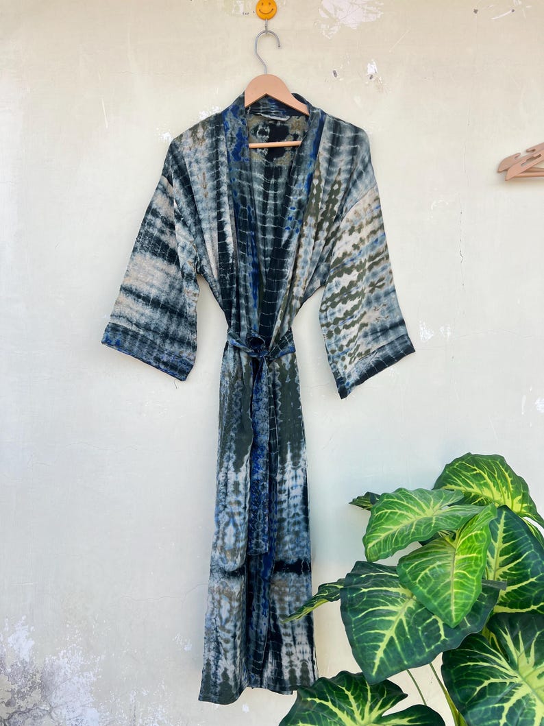 May include: A blue and green tie-dye silk robe with long sleeves and a sash tie. The robe is hanging on a wooden hanger against a white wall.