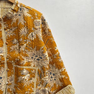 May include: A mustard yellow quilted jacket with a floral print and white stripes on the cuffs and pockets.