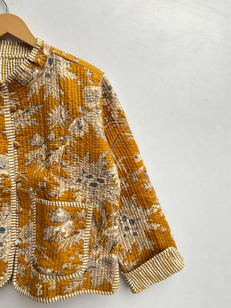 May include: A mustard yellow quilted jacket with a floral print and white stripes on the cuffs and pockets.