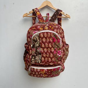 Può includere: Uno zaino trapuntato con un motivo floreale in tonalità di marrone, rosa e bianco. Lo zaino ha una tasca con cerniera sul davanti e una piccola tasca laterale.