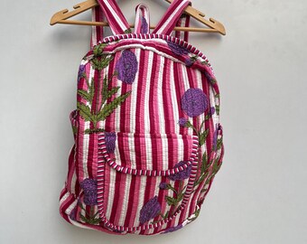 May include: A pink and white striped backpack with embroidered purple flowers. The backpack has a white trim and a zipper closure.