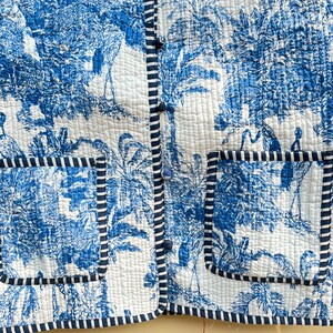 May include: A blue and white quilted jacket with a button-up front and two patch pockets. The jacket features a tropical print with palm trees and birds.