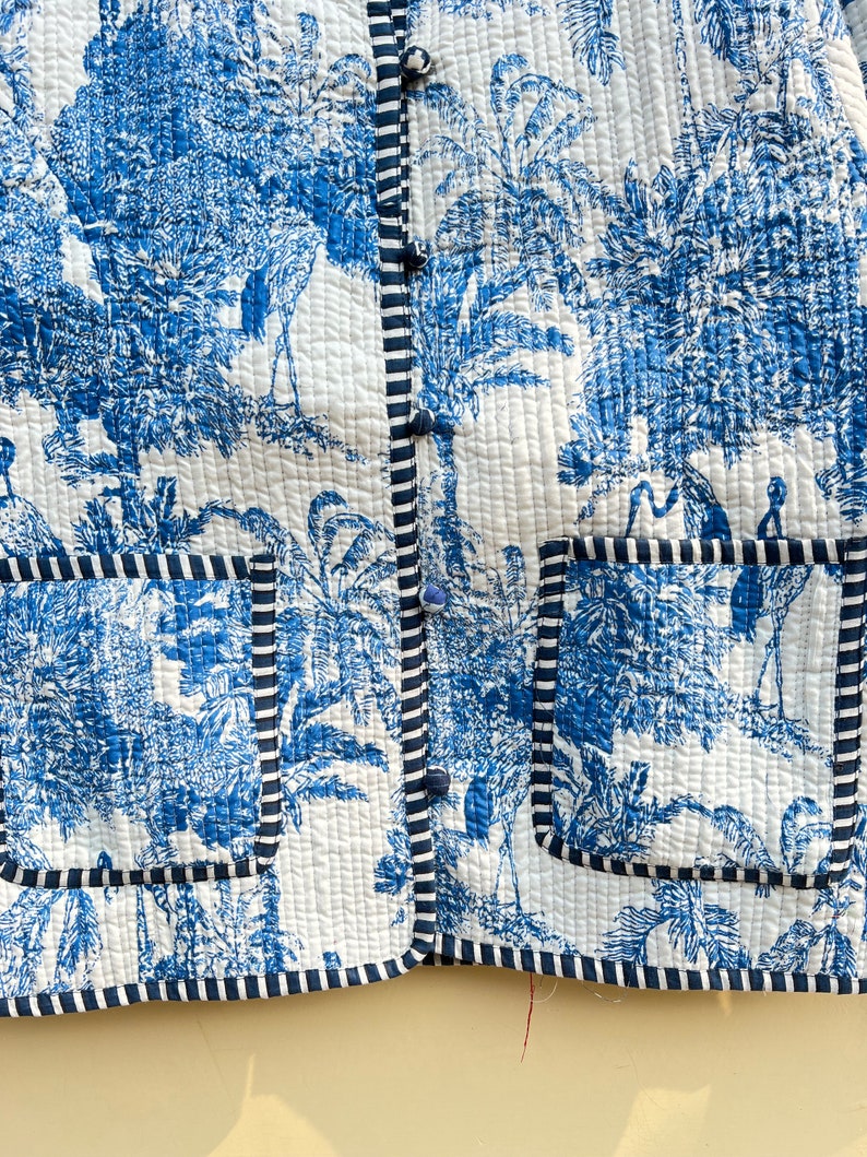 May include: A blue and white quilted jacket with a button-up front and two patch pockets. The jacket features a tropical print with palm trees and birds.