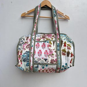 May include: A white patchwork tote bag with green and white striped trim. The bag has a floral print and is made of quilted fabric.