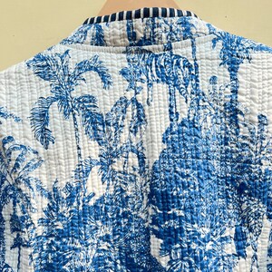 May include: A white quilted jacket with a blue and white tropical print featuring palm trees and animals. The jacket has a black and white striped trim around the collar.
