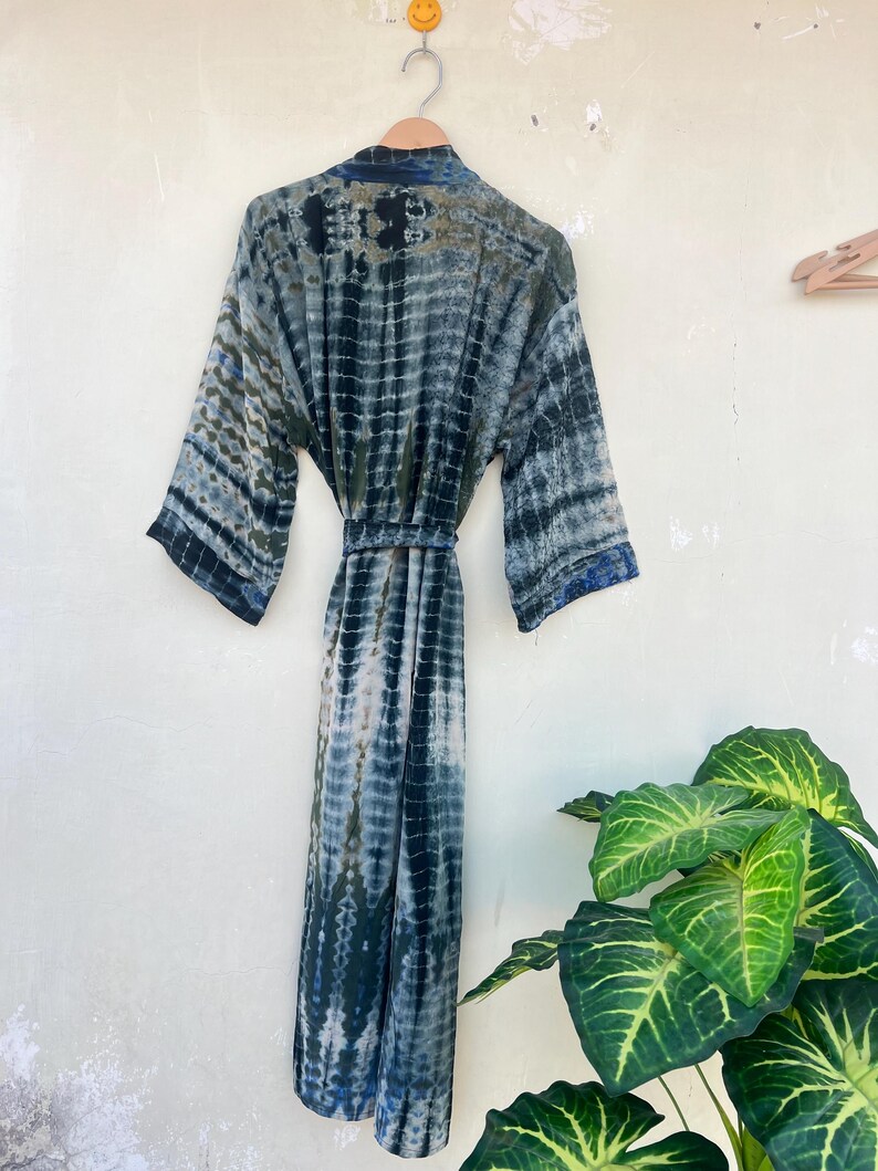K&ouml;nnte beinhalten: Eine lange, blaue und wei&szlig;e Batik-Robe mit einem G&uuml;rtel. Die Robe h&auml;ngt an einem Kleiderb&uuml;gel an einer wei&szlig;en Wand.