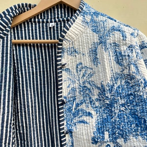 May include: A reversible quilted jacket with a blue and white striped pattern on one side and a blue and white floral pattern on the other side. The jacket has a mandarin collar and a button closure.