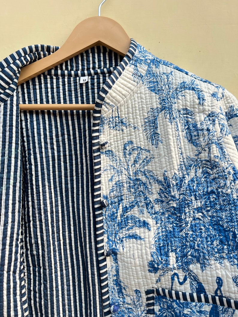 May include: A reversible quilted jacket with a blue and white striped pattern on one side and a blue and white floral pattern on the other side. The jacket has a mandarin collar and a button closure.