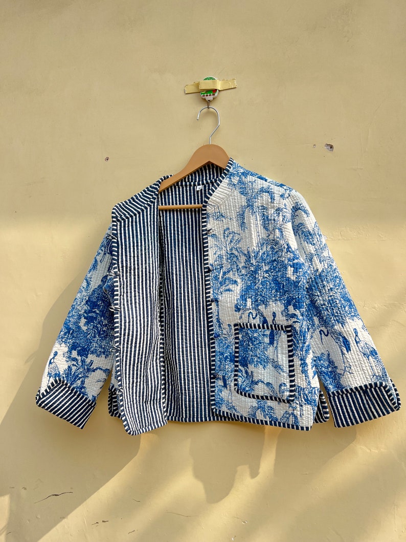 May include: A blue and white quilted jacket with a striped pattern on one side and a floral pattern on the other. The jacket has a pocket on the floral side.
