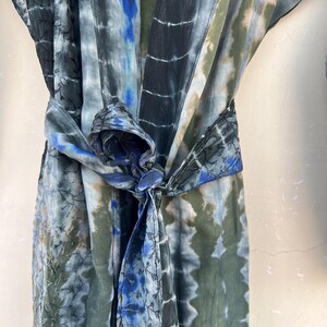 K&ouml;nnte beinhalten: Eine blaue und gr&uuml;ne Batik-Robe mit einem langen G&uuml;rtel, der in der Taille gebunden ist. Die Robe hat ein dezentes Stickmuster.