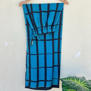 May include: A two-piece outfit, consisting of pants and a top, hangs on a wooden hanger. The fabric is a vibrant turquoise blue with a bold black grid pattern. The top has a gathered, elasticized cuff. The pants are long and straight-legged.