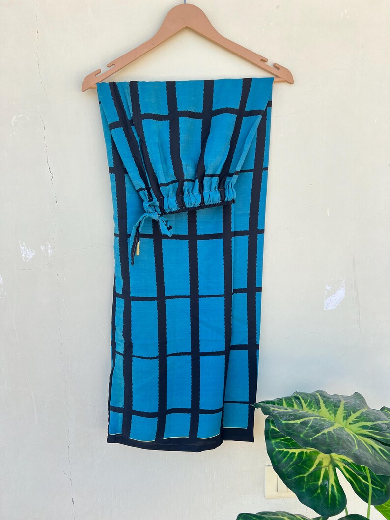 May include: A two-piece outfit, consisting of pants and a top, hangs on a wooden hanger. The fabric is a vibrant turquoise blue with a bold black grid pattern. The top has a gathered, elasticized cuff. The pants are long and straight-legged.