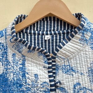 May include: A white quilted jacket with a blue and white striped lining. The jacket has a blue floral print and a single button closure. The size label says "M".