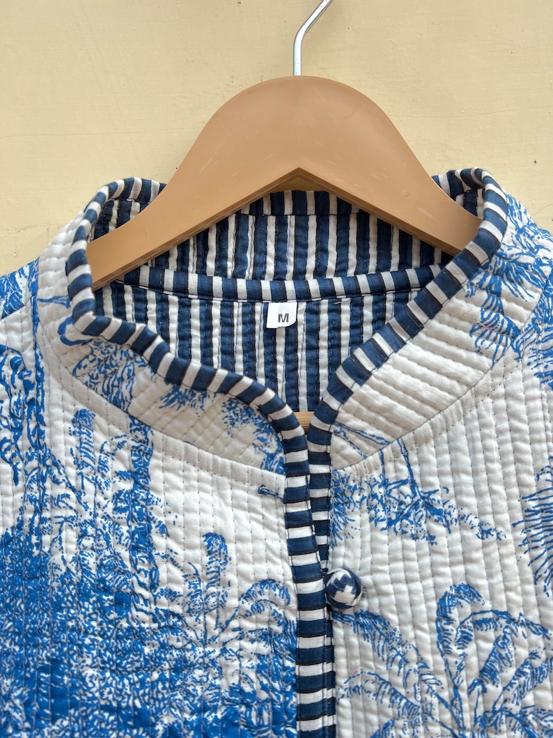 May include: A white quilted jacket with a blue and white striped lining. The jacket has a blue floral print and a single button closure. The size label says "M".