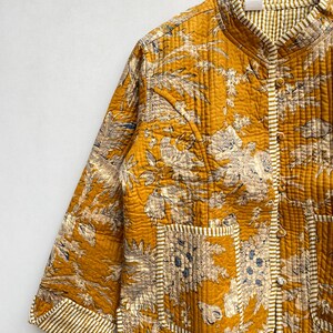 May include: A mustard yellow quilted jacket with a floral print and white piping. The jacket has a mandarin collar, a button closure, and two patch pockets.