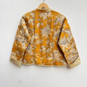 May include: A yellow quilted jacket with a floral print. The jacket has a mandarin collar and long sleeves with striped cuffs.