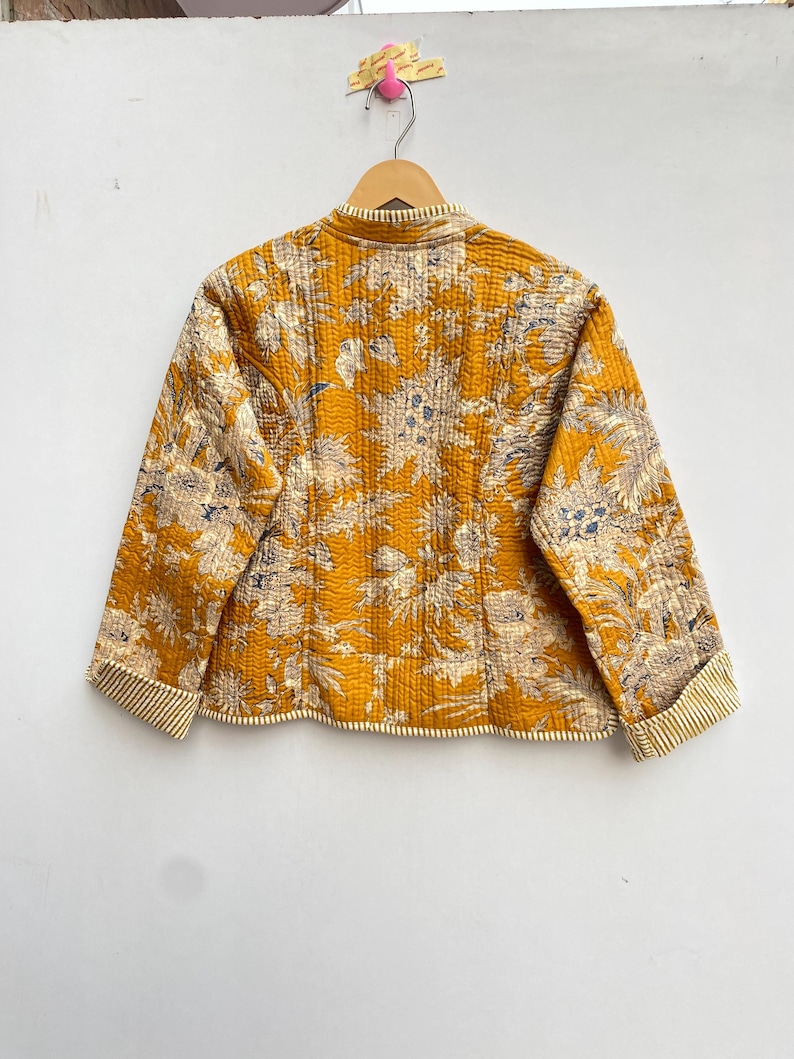 May include: A yellow quilted jacket with a floral print. The jacket has a mandarin collar and long sleeves with striped cuffs.