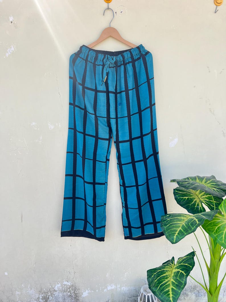 May include: Blue and black plaid patterned pants hanging on a wooden hanger. The pants have a drawstring waist and a wide leg design. The plaid pattern is made up of thick black lines on a blue background.