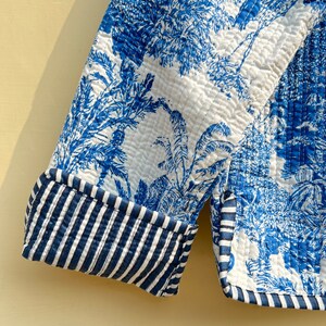 May include: A blue and white quilted jacket with a palm tree print. The jacket has a striped cuff detail.