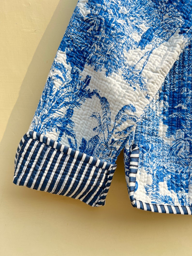 May include: A blue and white quilted jacket with a palm tree print. The jacket has a striped cuff detail.