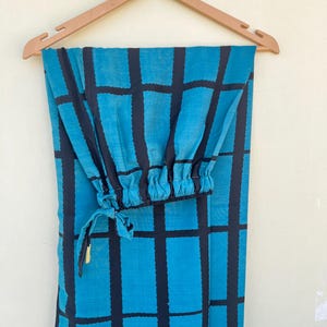 May include: A pair of teal and black patterned pants hanging on a wooden hanger. The pants feature a grid pattern in black over a teal background. The pants have an elastic cuff at the ankle and a drawstring.