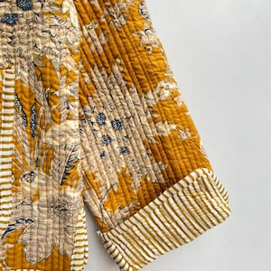 May include: A mustard yellow quilted jacket with a floral print and white and yellow striped cuffs.