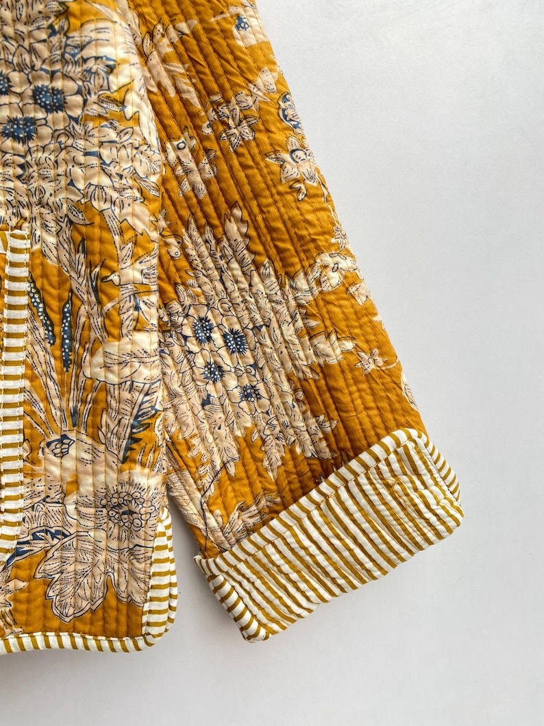 May include: A mustard yellow quilted jacket with a floral print and white and yellow striped cuffs.
