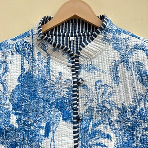 May include: A white quilted jacket with a blue and white floral print. The jacket has a mandarin collar and a button closure. The lining is a blue and white striped fabric. The size tag says "M".