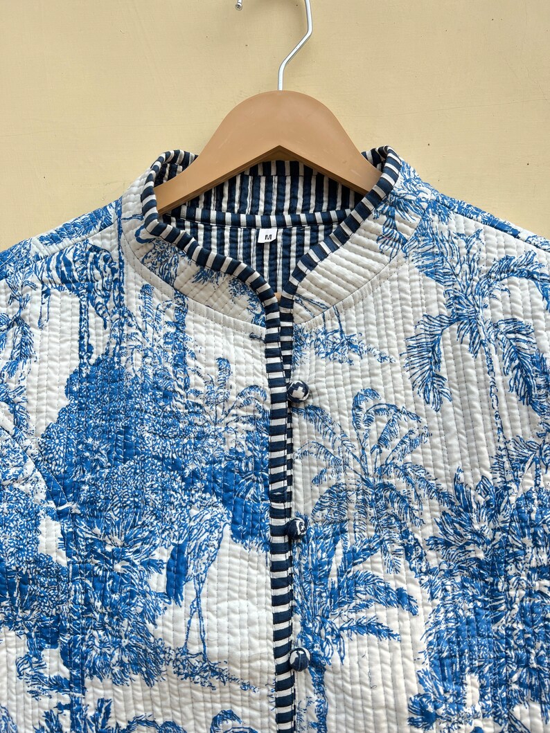May include: A white quilted jacket with a blue and white floral print. The jacket has a mandarin collar and a button closure. The lining is a blue and white striped fabric. The size tag says "M".