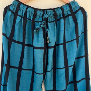 May include: A pair of blue and black patterned pants hanging on a wooden hanger. The pants feature a grid design with thick black lines on a blue background. The waistline has a drawstring closure.