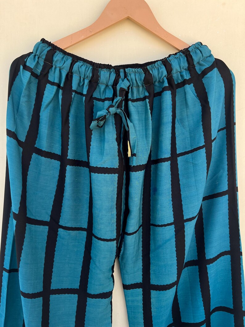 May include: A pair of blue and black patterned pants hanging on a wooden hanger. The pants feature a grid design with thick black lines on a blue background. The waistline has a drawstring closure.