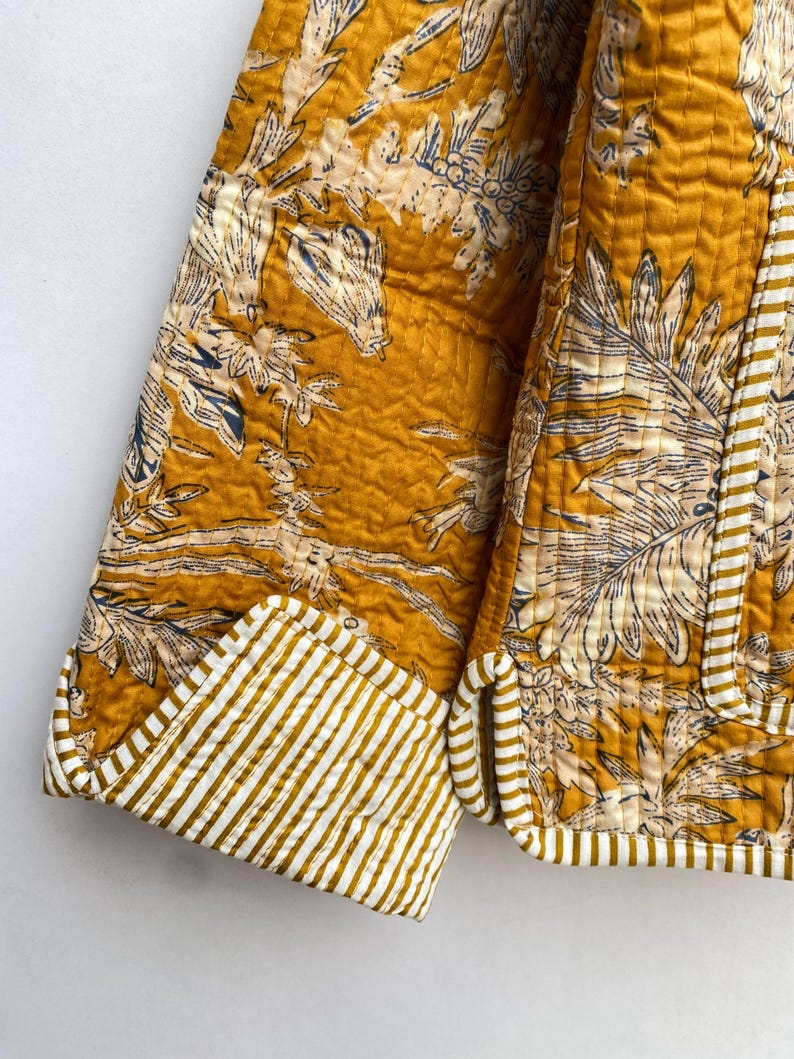 May include: A mustard yellow quilted jacket with a white and blue floral print. The jacket has a striped cuff detail.