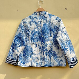 May include: A white quilted jacket with a blue and white print of palm trees and animals. The jacket has a mandarin collar and a striped trim on the cuffs and hem.