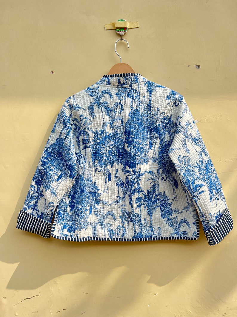 May include: A white quilted jacket with a blue and white print of palm trees and animals. The jacket has a mandarin collar and a striped trim on the cuffs and hem.