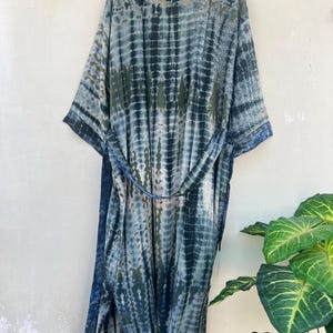 K&ouml;nnte beinhalten: Eine lange, blaue und gr&uuml;ne Batik-Robe mit einem G&uuml;rtel. Die Robe hat eine lockere Passform und ist aus einem weichen, flie&szlig;enden Stoff gefertigt.