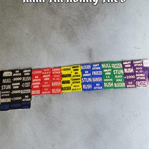 May include: A collection of colorful Mini Tin Ability Tiles with various game effects and text. The tiles are arranged in a row, with text such as "Freeze", "Stun", and "Rush". The text "Mini Tin Ability Tiles" is at the top.