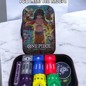 May include: A TCG Mini Tin Insert featuring a One Piece Card Game design. The tin displays a character illustration and the game's logo. Inside, there are various colored game pieces and tokens, including dice and markers, with the text "RetroJoe3D".