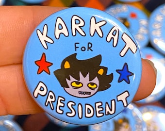 May include: A blue button with white text that reads "Karkat for President" and features a cartoon character with black hair and yellow eyes. The button has two red stars and one blue star.