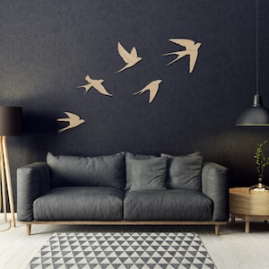 May include: A modern living room with a dark gray sofa, wooden side table, and a patterned rug. Five wooden swallows are mounted on the dark wall. A floor lamp and pendant light complete the decor.