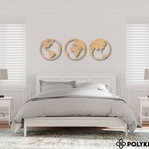 May include: Three wooden wall decorations shaped like the Earth, each showing a different continent. The decor is displayed on a white wall above a white bed with grey bedding.