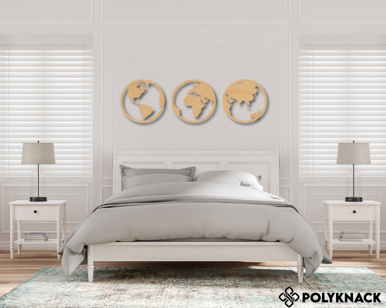 May include: Three wooden wall decorations shaped like the Earth, each showing a different continent. The decor is displayed on a white wall above a white bed with grey bedding.