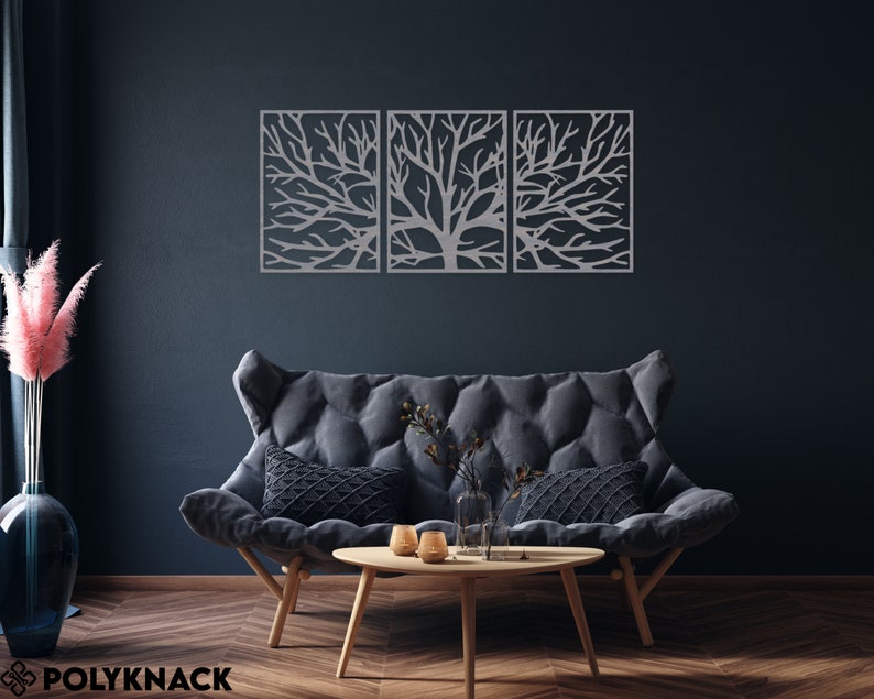 May include: Three-piece metal wall art featuring a tree branch design. The artwork is silver and mounted on a dark blue wall above a gray sofa. The room is decorated with a wooden coffee table and a vase with pink flowers.