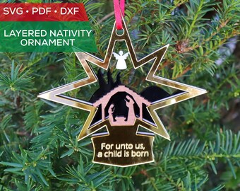 May include: A gold star-shaped Christmas ornament with a layered nativity scene inside. The ornament features a brown manger with a black silhouette of Mary, Joseph, and the baby Jesus. The text "For unto us, a child is born" is written on the bottom of the ornament.