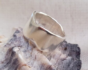 May include: A silver ring with an organic, wavy design. The ring is sitting on a textured, gray and white seashell.