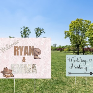 May include: Two wedding signs, one with a pink and white background and the other with a blue and white background. The pink sign says "Welcome Ryan & Emma" with a cowboy hat and boots. The blue sign says "Wedding Parking" with an arrow pointing to the right.
