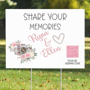 May include: White wedding sign with the text "Share Your Memories Ryan & Ellen" in pink script. A watercolour illustration of a camera with flowers is on the left. A pink QR code is on the right with the text "Your QR Wedding Code".